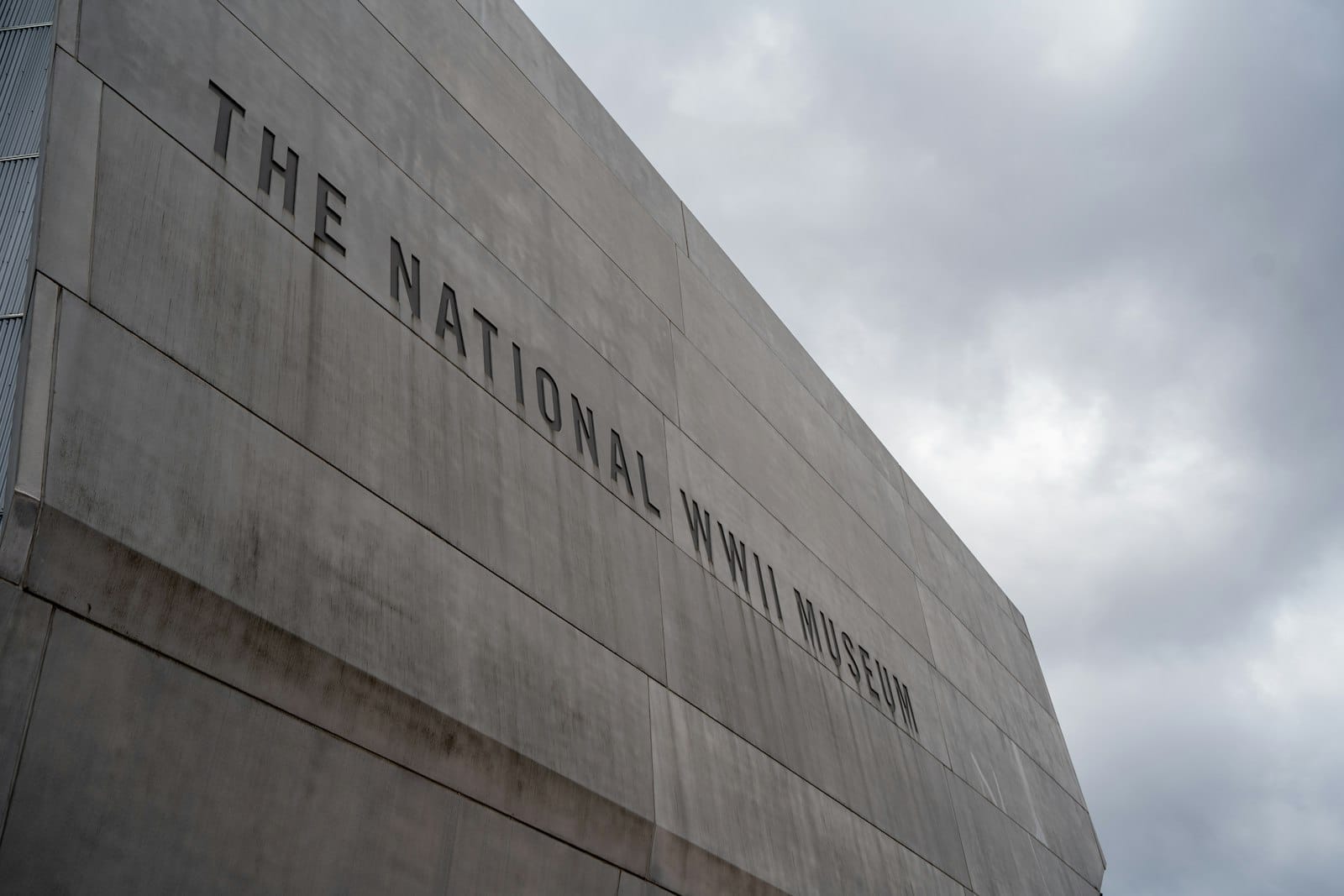 O exterior de concreto do The National WWII Museum em New Orleans sob um céu nublado, com grandes letras visíveis no edifício.