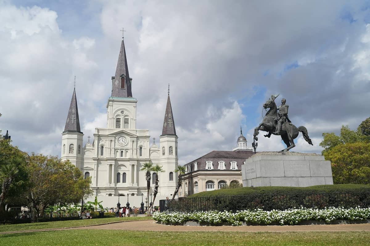 Stately view of the Cabildo and St. Louis Cathedral with Jackson Square and equestrian statue in foreground, under a cloudy sky in New Orleans.