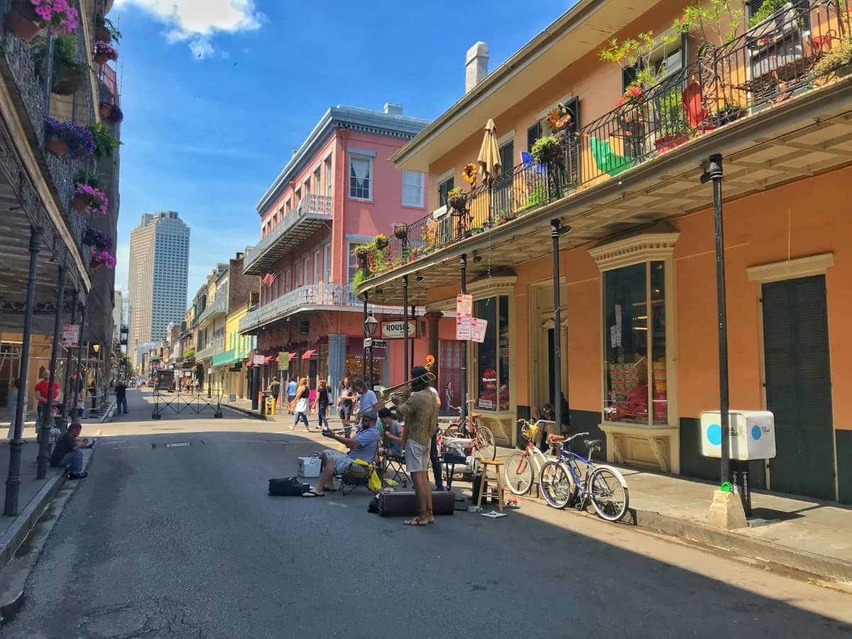 Street scene in New Orleans French Quarter with musicians performing for a crowd and colorful historic buildings in the background.