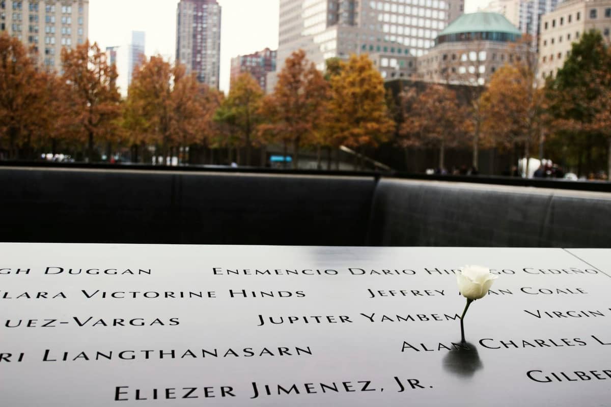 Nahaufnahme des 9/11 Memorial in New York City mit eingemeißelten Namen, einer einzelnen weißen Rose und Herbstbäumen im Hintergrund.