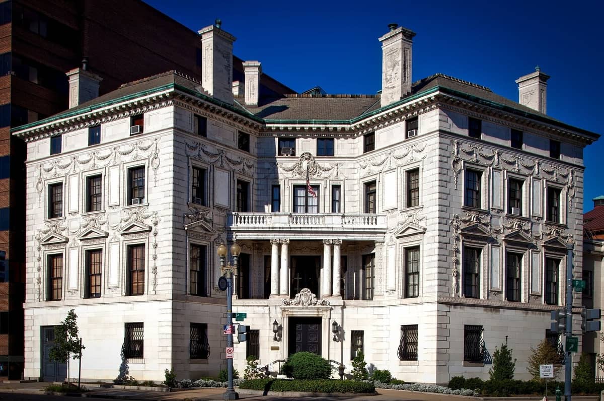 Historisches Herrenhaus mit verzierter Fassade, großen Fenstern und klassischen Architekturdetails, umgeben von Stadtgebäuden an einem klaren Tag.