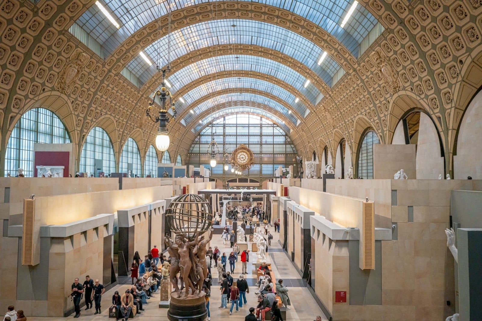 Vista panoramica della grande sala a volta del Musée d'Orsay, piena di visitatori, sculture e luce naturale che filtra attraverso il soffitto in vetro ad arco.