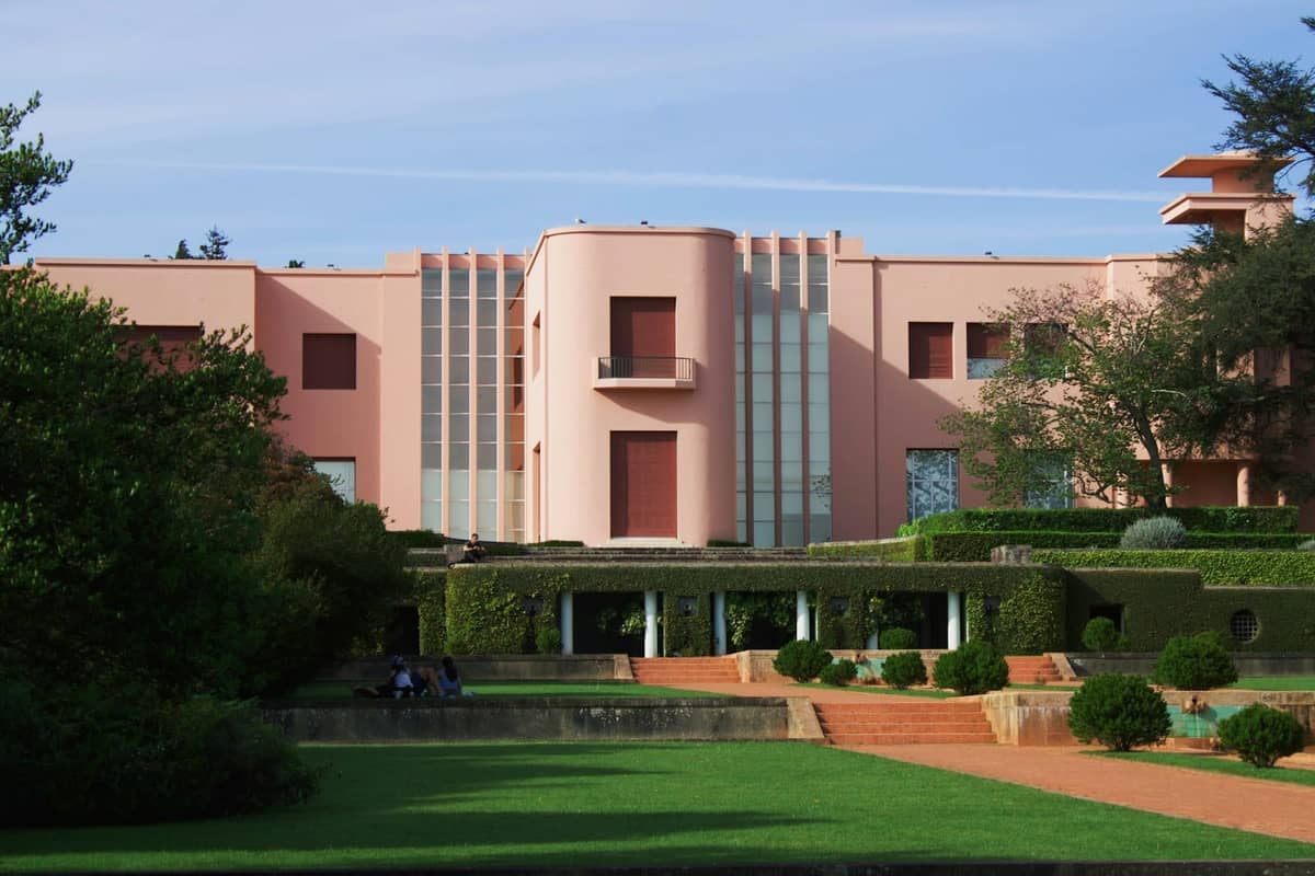 Różowa fasada Art Déco Muzeum Serralves, otoczona zadbanymi ogrodami pod błękitnym niebem w Porto, Portugalia.