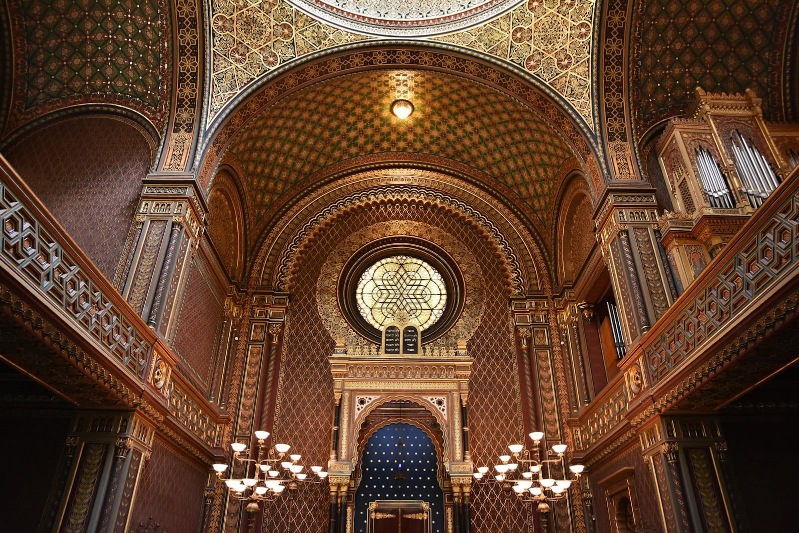 Interior elegante em estilo mourisco da Sinagoga Espanhola de Praga com teto ornamentado, vitral e arcos decorativos.