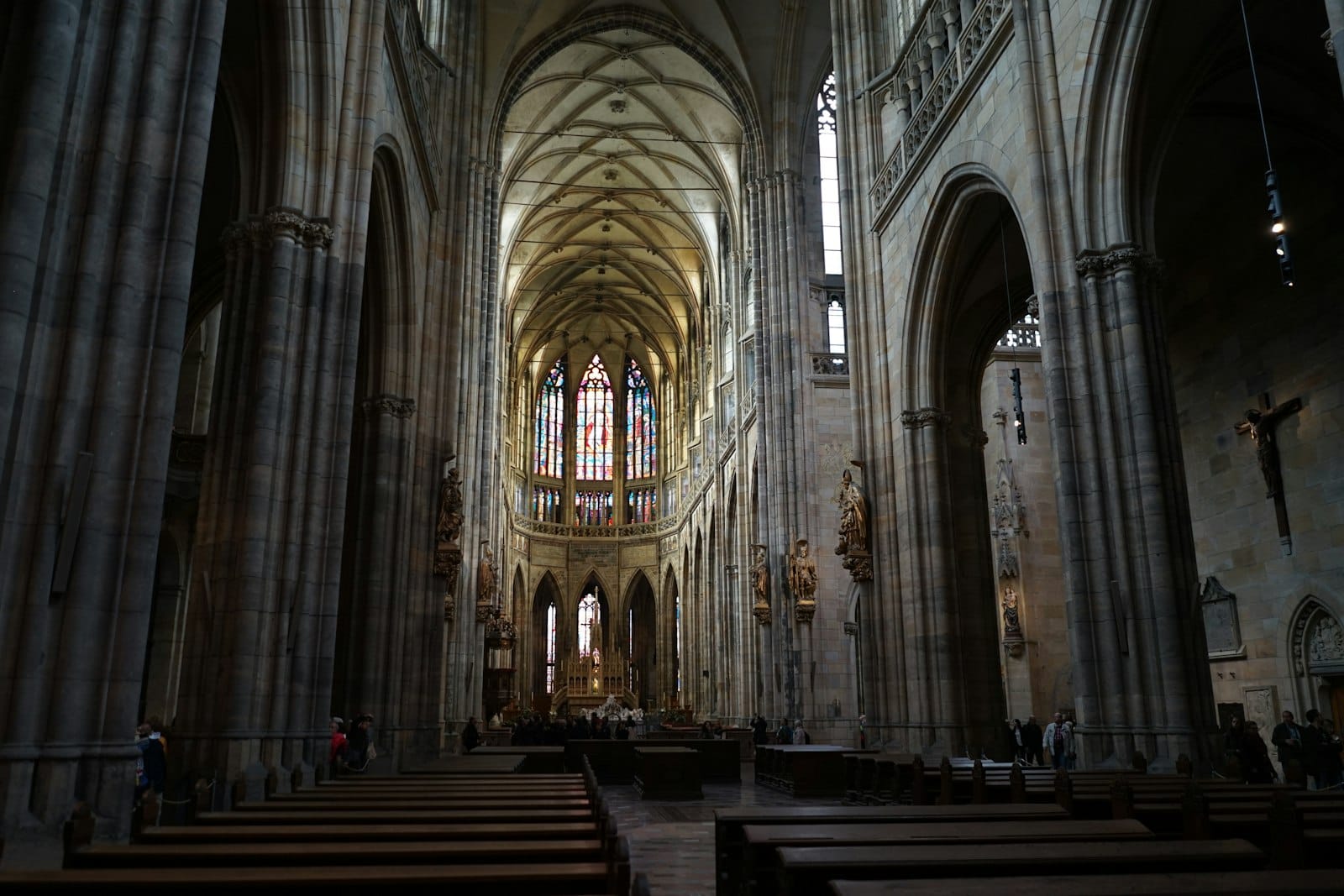 Vista interior de uma grande catedral gótica com altos tetos abobadados, arcos, bancos e coloridos vitrais.