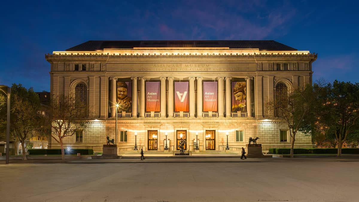 Frontansicht des Asian Art Museum in San Francisco in der Abenddämmerung, mit Bannern und beleuchtetem Eingang.