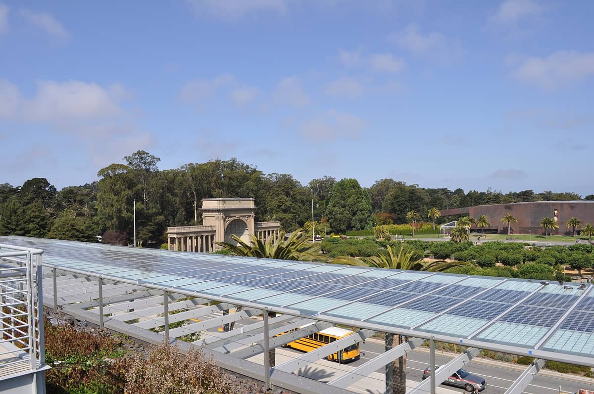 Landschaftsansicht des Golden Gate Park mit der California Academy of Sciences und dem nahe gelegenen Music Concourse, mit Sonnenkollektoren im Vordergrund und Bäumen im Hintergrund.