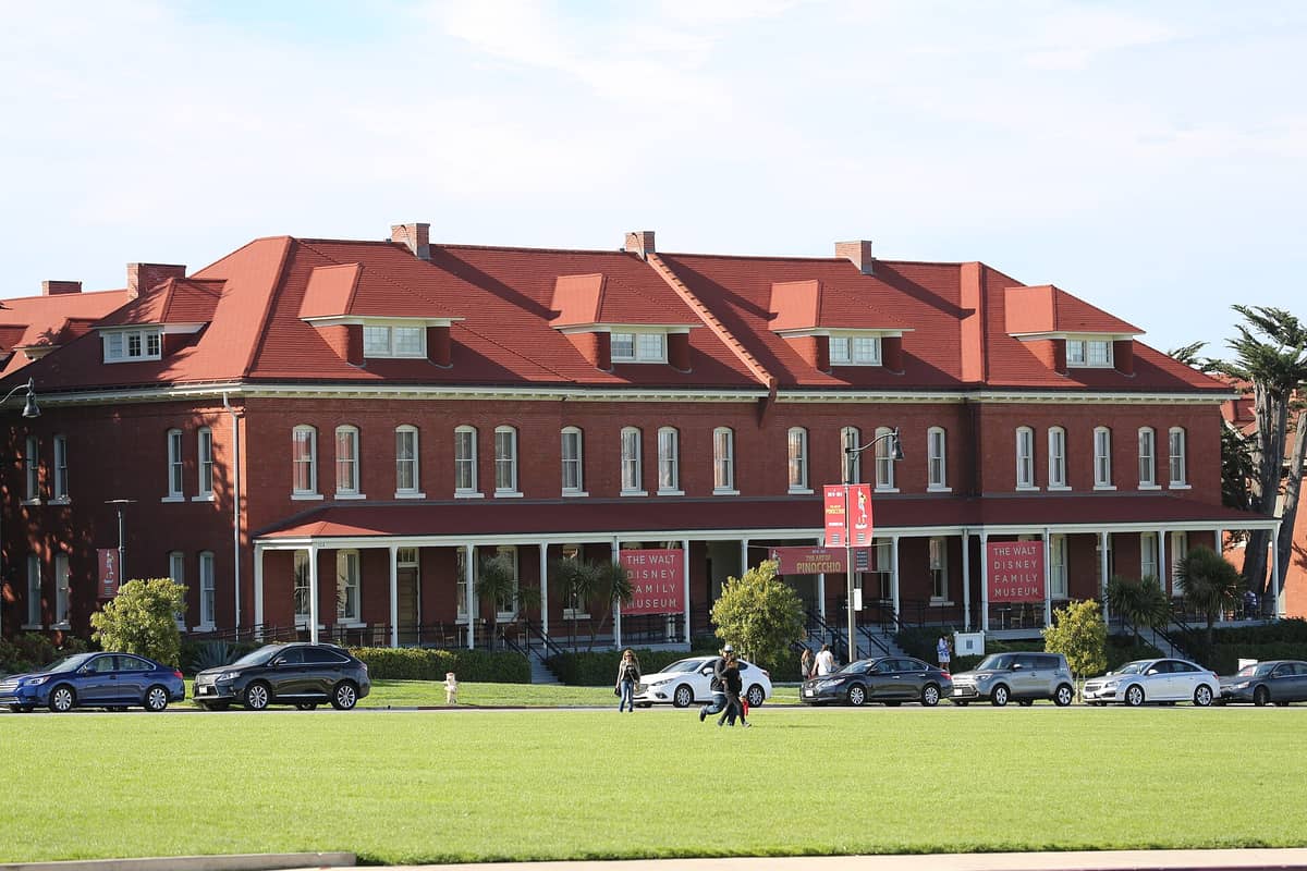 Das Walt Disney Family Museum in San Francisco, ein Backsteingebäude mit einem leuchtend roten Dach, davor parkende Autos und einem grünen Rasen.