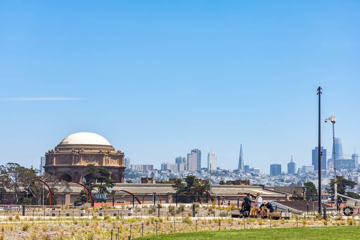 Weitwinkelansicht des Palace of Fine Arts mit Familien im Vordergrund und der Skyline von San Francisco im Hintergrund an einem sonnigen Tag.