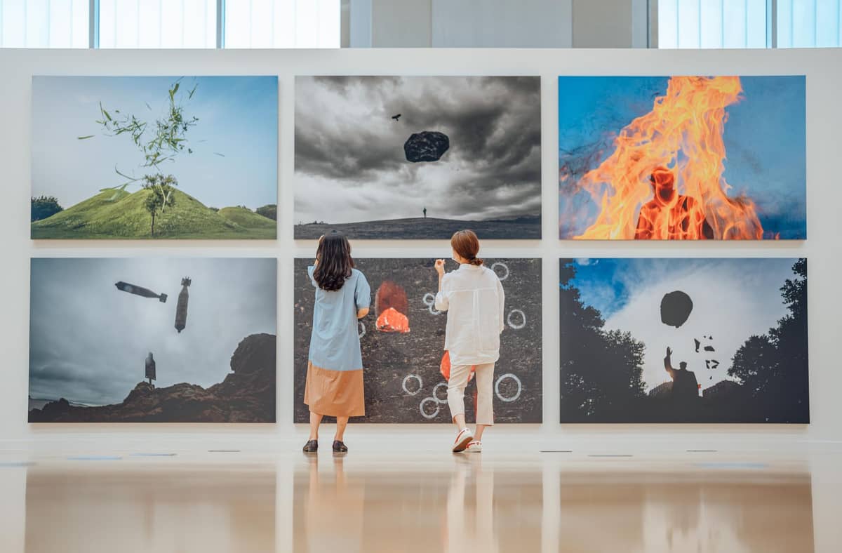 Duas pessoas observando uma parede de grandes fotografias contemporâneas em uma galeria de museu moderno e iluminado.