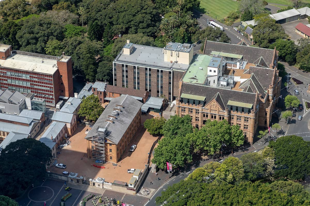 Aerial view of Sydney's UNESCO-listed Hyde Park Barracks, a historic convict-era building surrounded by trees and adjacent modern buildings.