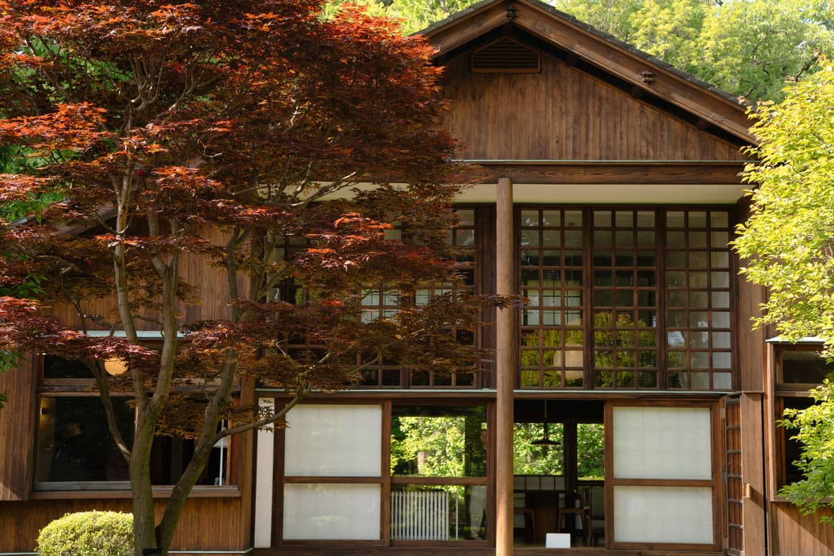 Exterior view of a preserved wooden Japanese building surrounded by green trees, typical of those at Edo-Tokyo Open Air Architectural Museum.