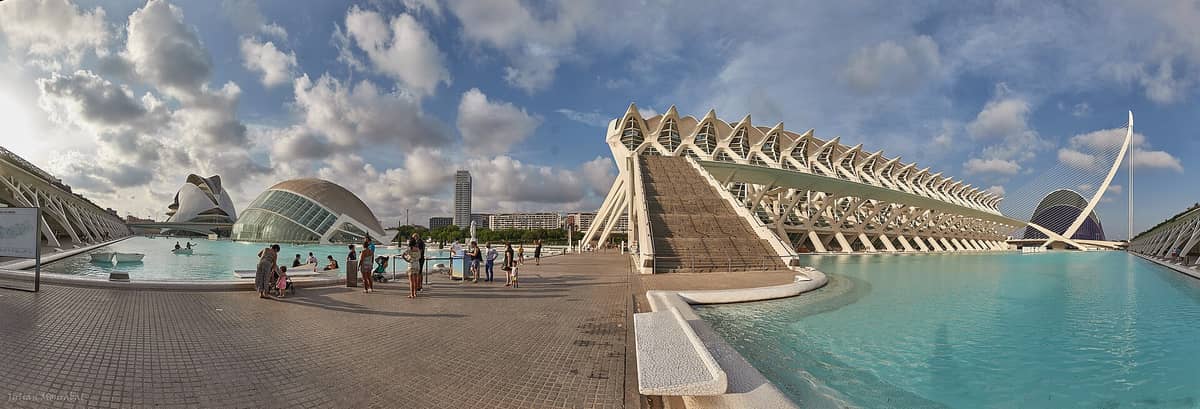 Weites Panorama der Ciudad de las Artes y las Ciencias in Valencia mit moderner Architektur, Glasgebäuden, Wasserbecken und Besuchern, die den Platz genießen.