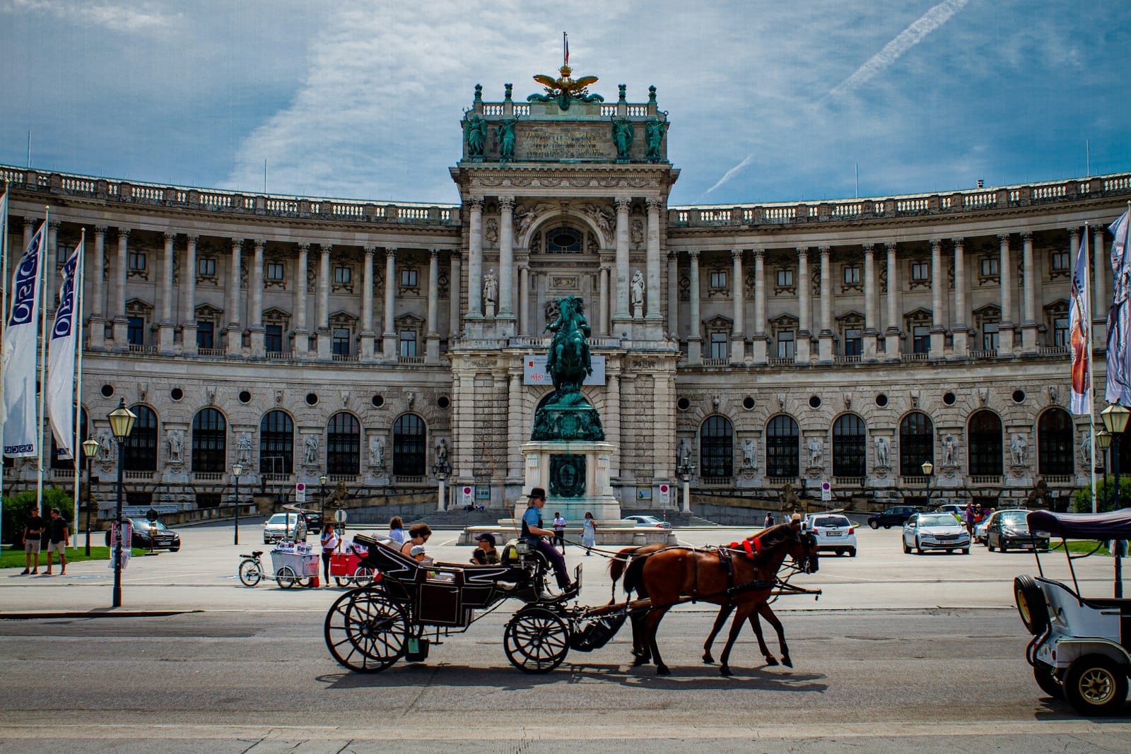 Szeroki widok na fasadę Pałacu Hofburg w Wiedniu z posągiem i powozem zaprzężonym w konie na pierwszym planie, ilustrujący historię cesarską.