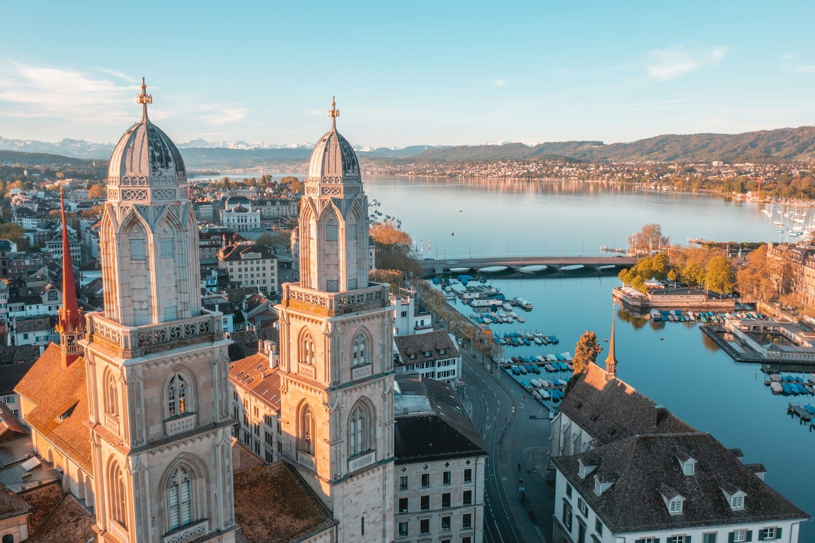 มุมสูงของยอดโบสถ์ Grossmünster กลางเมืองซูริค โดยมีทะเลสาบซูริคและฉากเมืองรายล้อม ถ่ายในแสงแดดนุ่มนวล