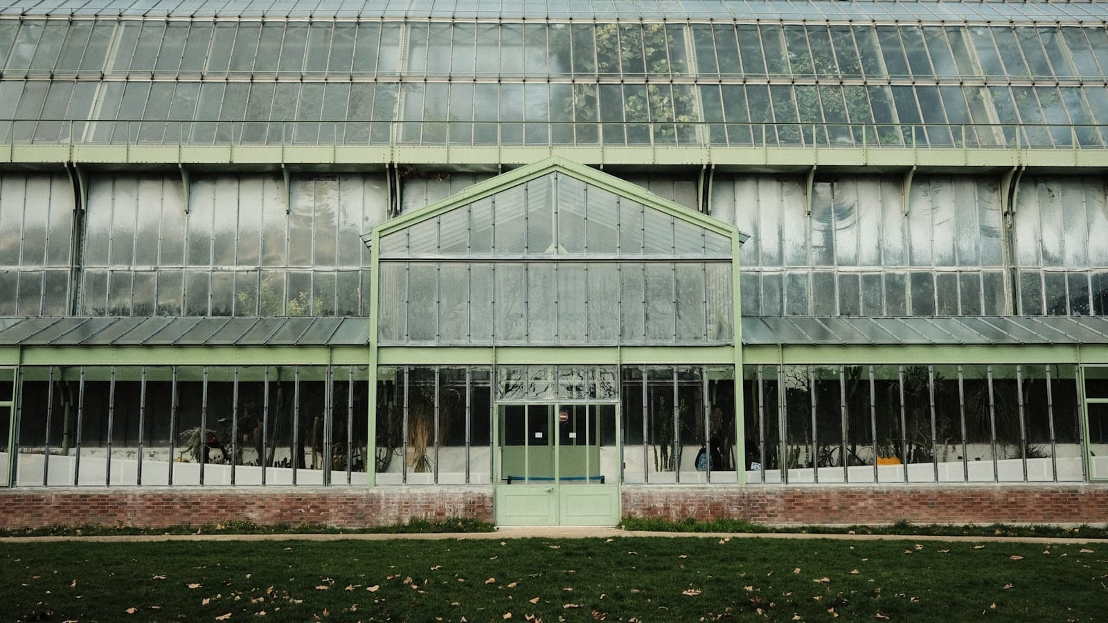 Fassade eines großen Glasgewächshauses mit einem grünen Rasen davor, Teil des Jardin des Plantes in Paris.
