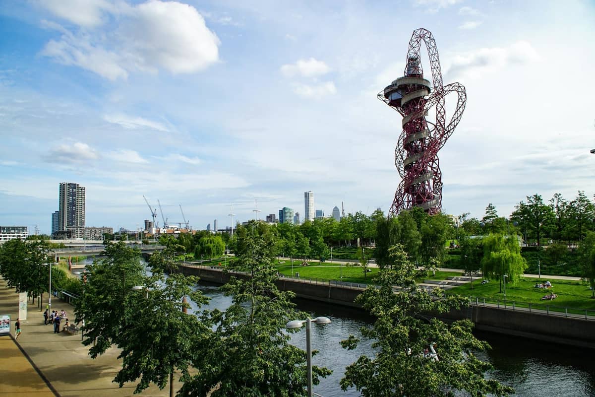 Vista do Queen Elizabeth Olympic Park no leste de Londres, com a escultura ArcelorMittal Orbit, espaços verdes, árvores, rio e pessoas relaxando ao ar livre.