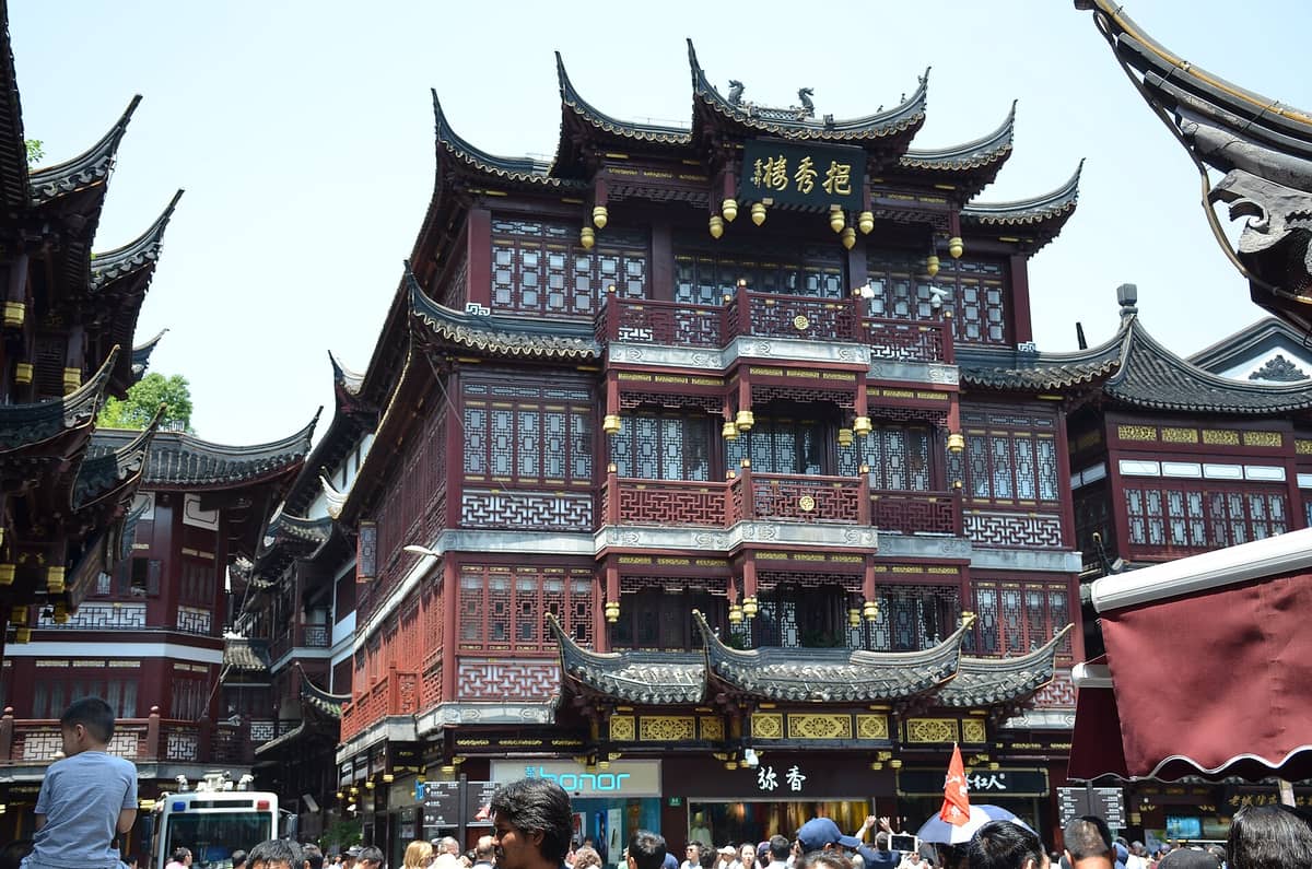 Gran multitud frente a edificios tradicionales chinos con ornamentados detalles en rojo y dorado en el Casco Antiguo de Shanghái cerca del Jardín Yu en un día soleado.