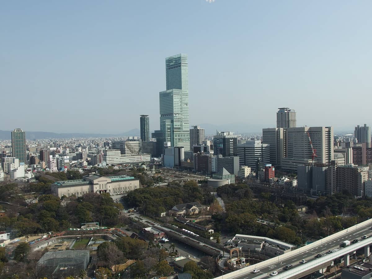 Daytime cityscape of Osaka showing Abeno Harukas skyscraper, Tennoji Park, and abundant greenery with nearby urban buildings.