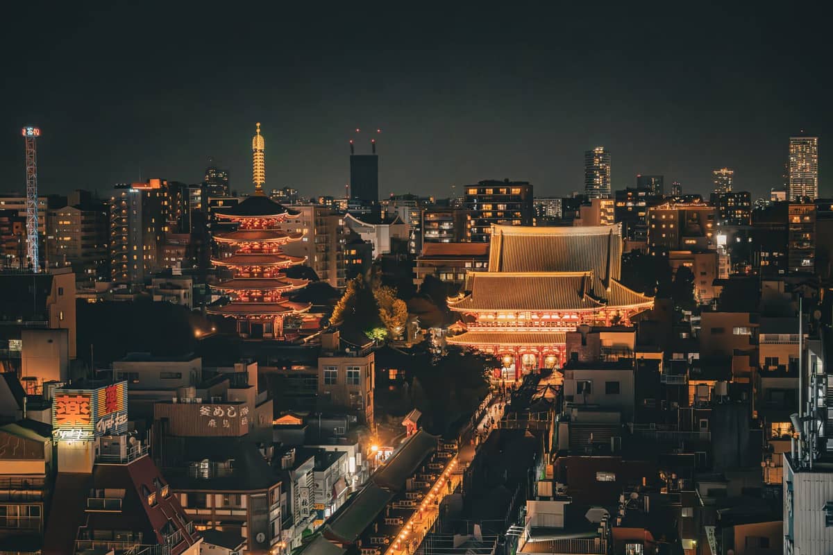 Night view of Senso-ji Temple with its pagoda and main hall illuminated, surrounded by city lights in Tokyo.