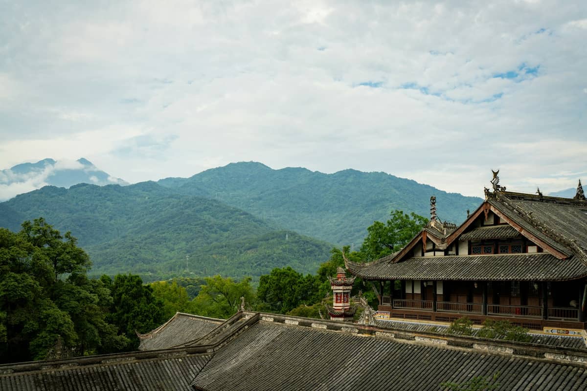 Panoramablick auf ein altes taoistisches Kloster mit geschwungenen Ziegeldächern vor üppig grünen Bergen in der Nähe von Chengdu.