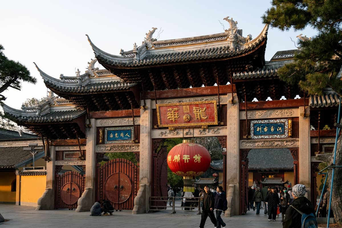 Il sontuoso portale d'ingresso di un tempio taoista a Shanghai, con persone che camminano e una grande lanterna rossa appesa sopra l'entrata.