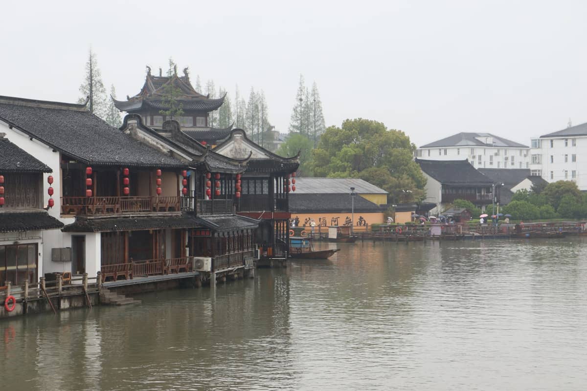 Edifici cinesi tradizionali con tetti in stile pagoda accanto a un fiume in un'atmosfera nebbiosa fuori dal centro di Shanghai.