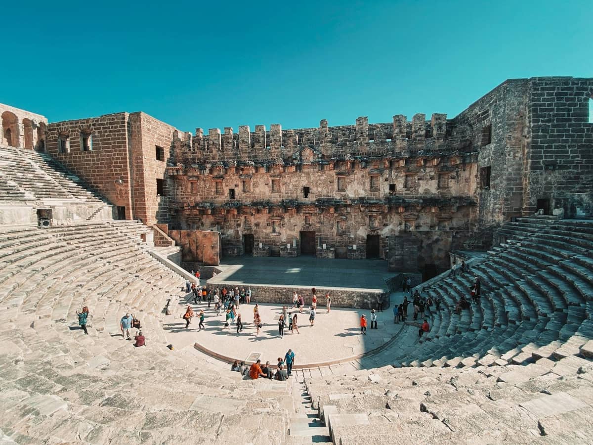 Wide view of Antalya's ancient Roman theater with visitors exploring under clear spring skies.