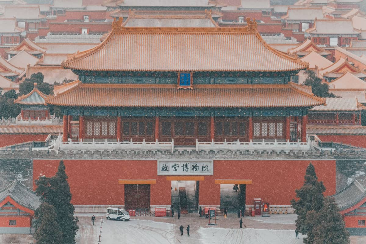 La porte principale de la Cité Interdite de Beijing saupoudrée de neige avec de légères chutes de neige, se détachant sur les murs rouges et les toits dorés, évoquant une atmosphère hivernale paisible.