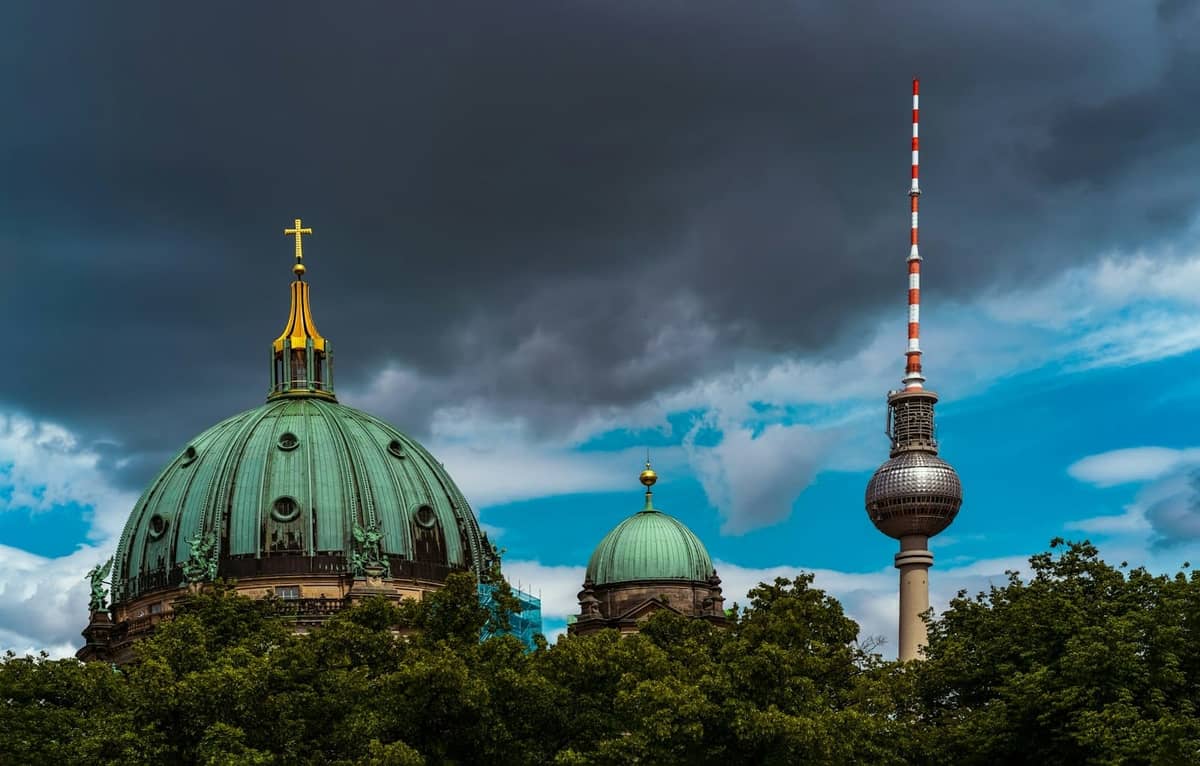 Berliner Dom und Fernsehturm unter einem dramatischen, teilweise bewölkten Himmel, der die Skyline der Stadt und das wechselhafte Wetter zeigt.