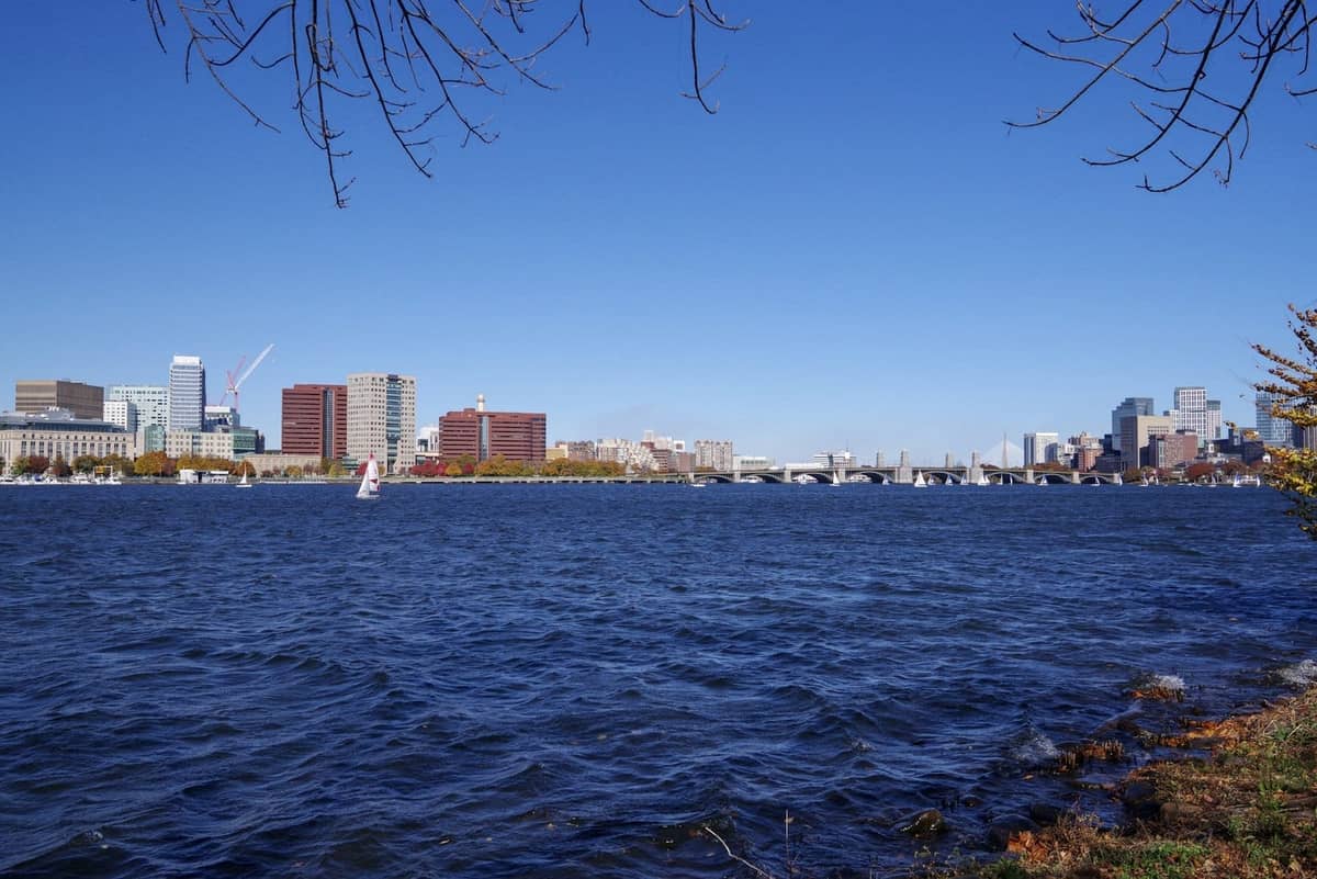 Panorama Bostonu jesienią z bezchmurnym błękitnym niebem, budynkami miasta, rzeką Charles i drzewami w jesiennych barwach nad wodą.