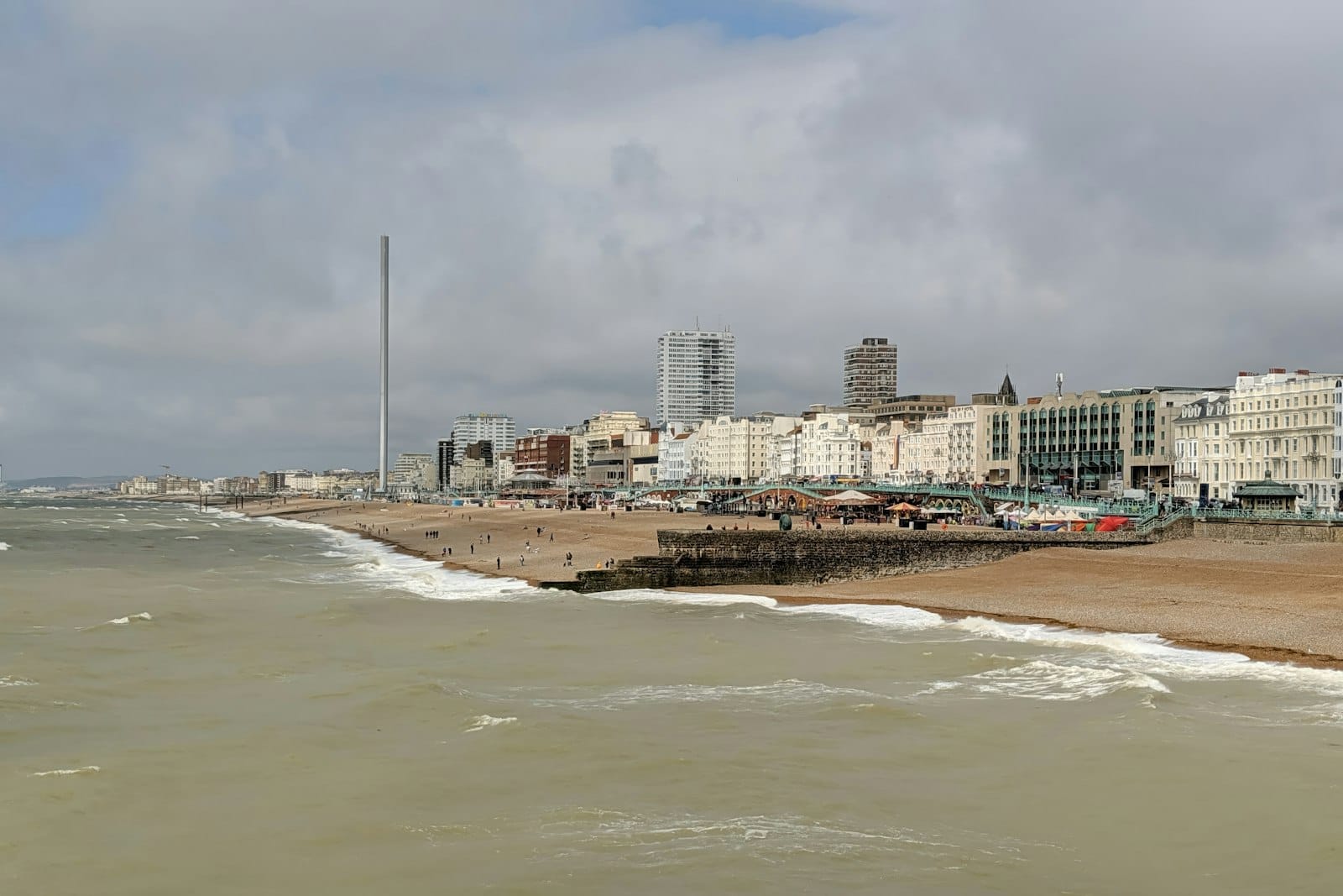 Cielo nublado sobre la playa y el paseo marítimo de Brighton con olas y edificios, mostrando el típico clima marítimo templado de la ciudad.