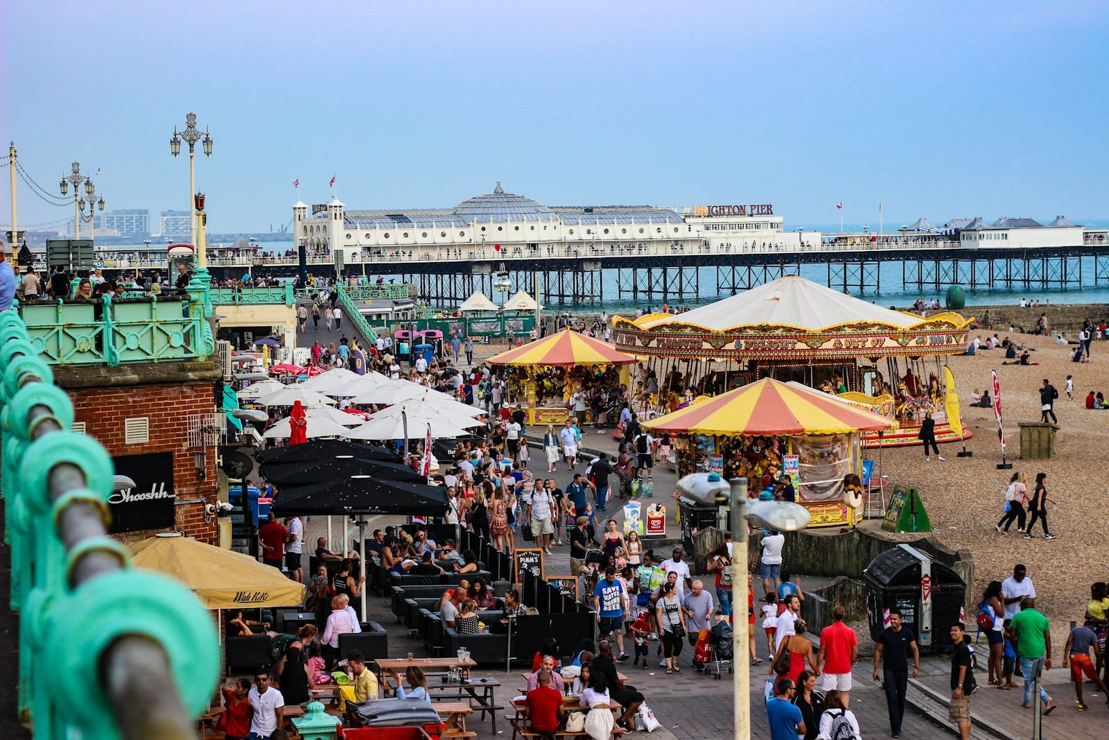 Multitudes disfrutando del paseo marítimo de Brighton con el muelle y el carrusel, ilustrando el animado ambiente de un festival o evento.