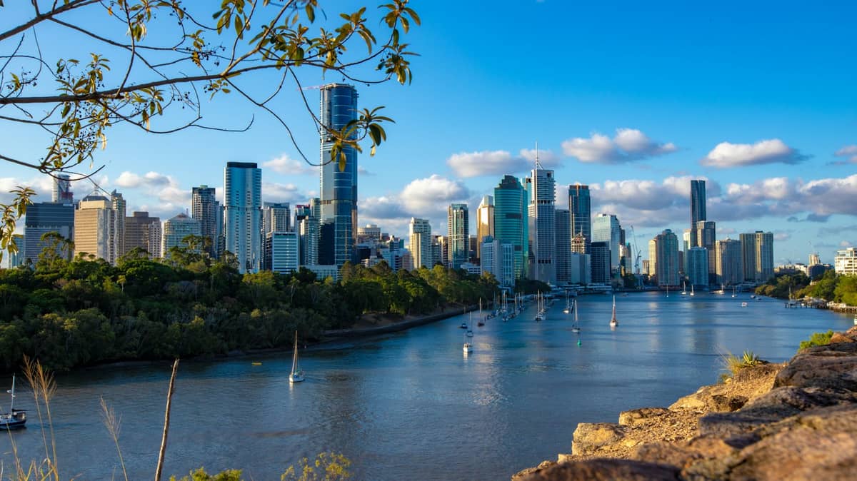 Tagesansicht der Skyline von Brisbane mit modernen Wolkenkratzern und dem Brisbane River unter einem teilweise bewölkten blauen Himmel.