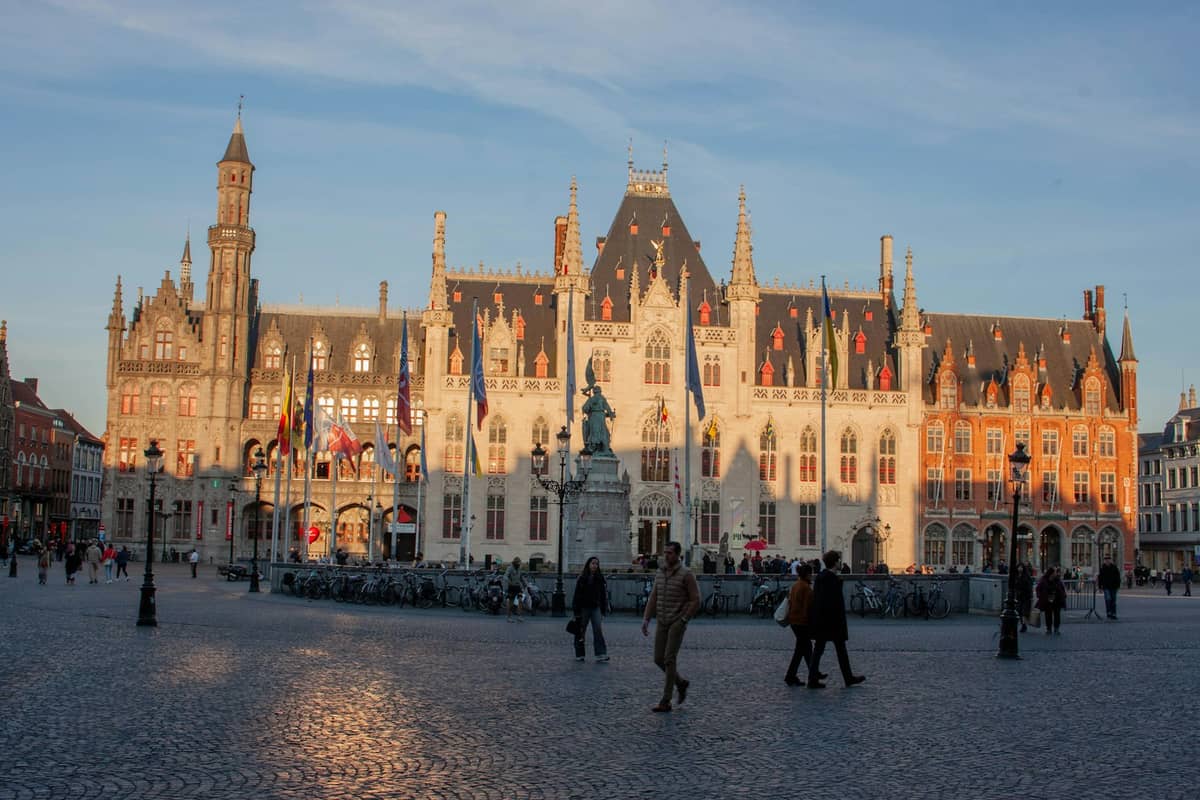 People walk across Bruges' Markt square in front of the historic Provincial Court building on a winter day