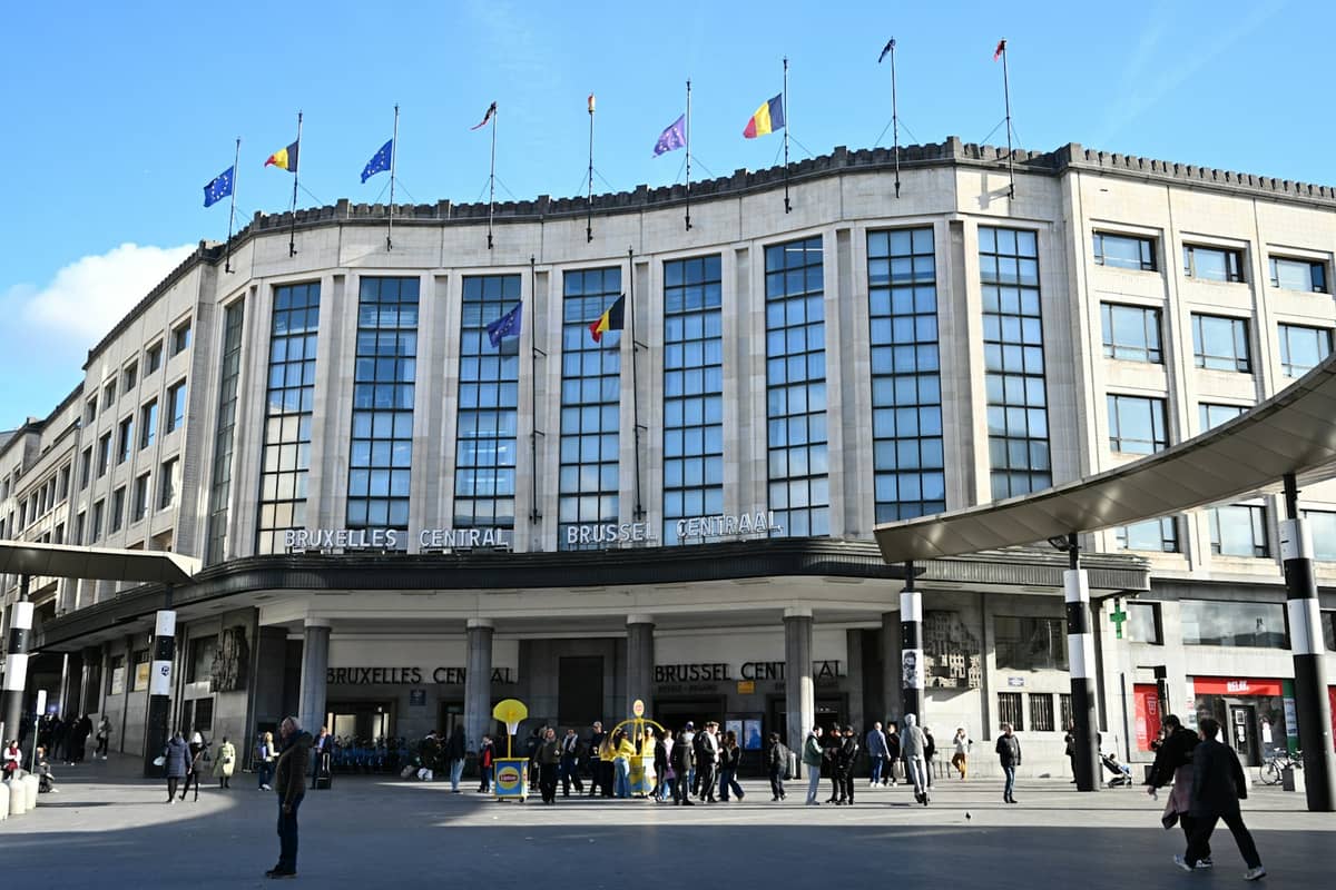 Vista exterior da estação de trem Brussels Central com pessoas caminhando do lado de fora em um dia ensolarado.