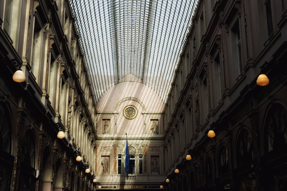 Interior das Galeries Royales Saint-Hubert em Bruxelas com teto de vidro, arquitetura ornamentada e iluminação suave.