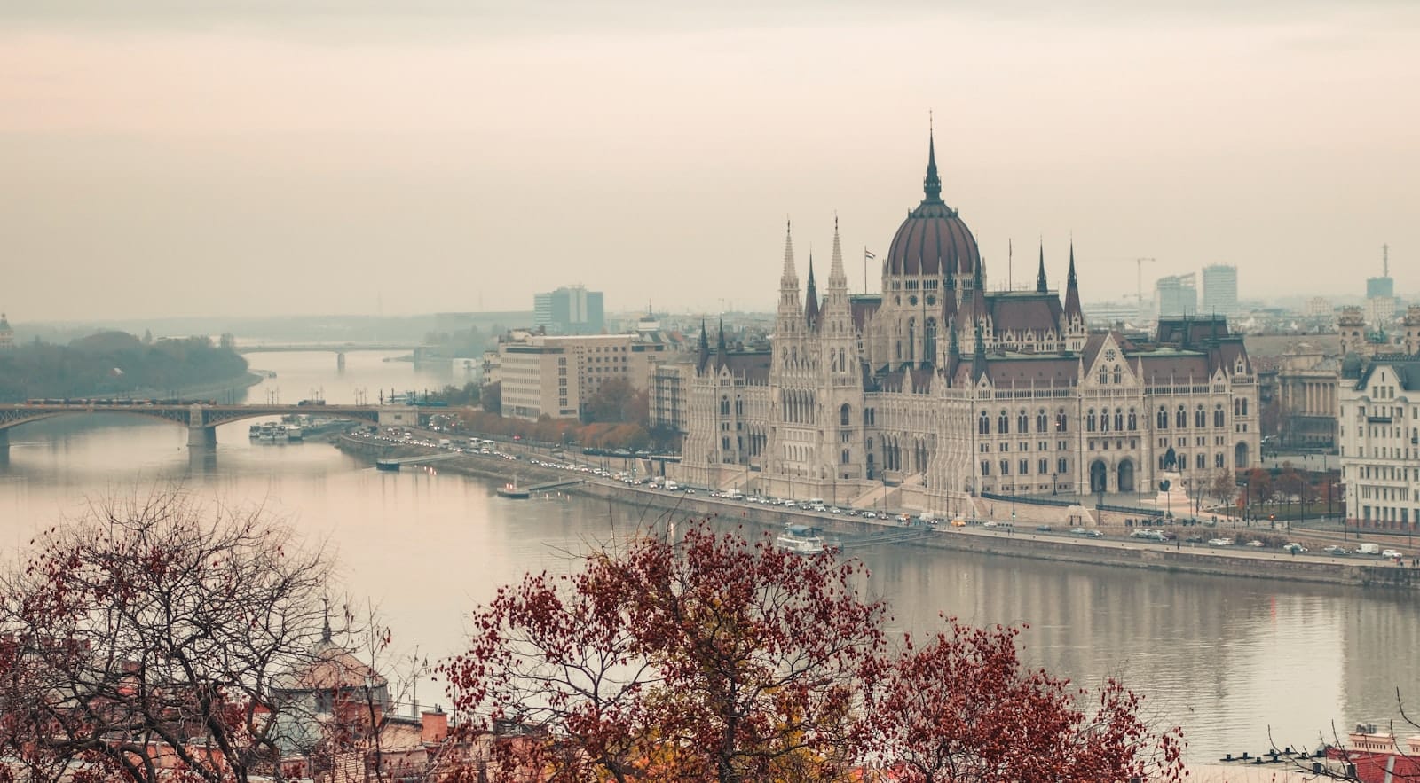 Budapest Parliament and Danube view in autumn with colorful foliage in the foreground under a cloudy sky.