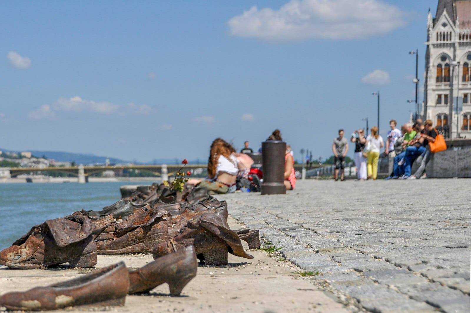 People sitting along the Danube promenade near the Shoes on the Danube Bank memorial in Budapest on a sunny day.