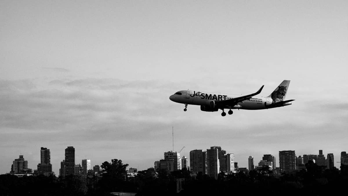 ภาพขาวดำของเครื่องบิน JetSmart กำลังลงจอดโดยมีเส้นขอบฟ้าของเมือง Buenos Aires เป็นฉากหลัง