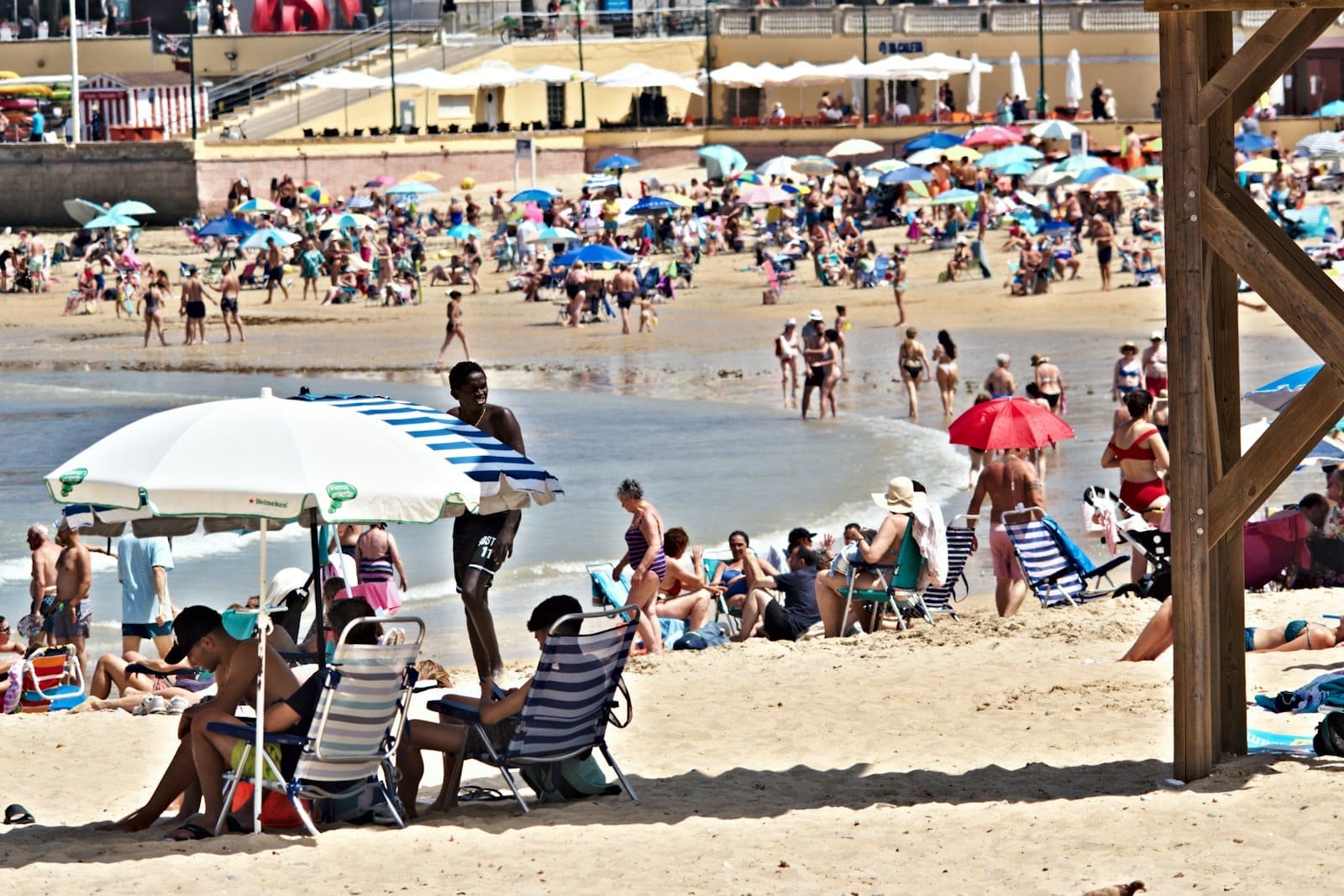 Movimentada cena de praia em Cádiz com muitas pessoas, guarda-sóis coloridos e banhistas, capturando a animada atmosfera de verão.