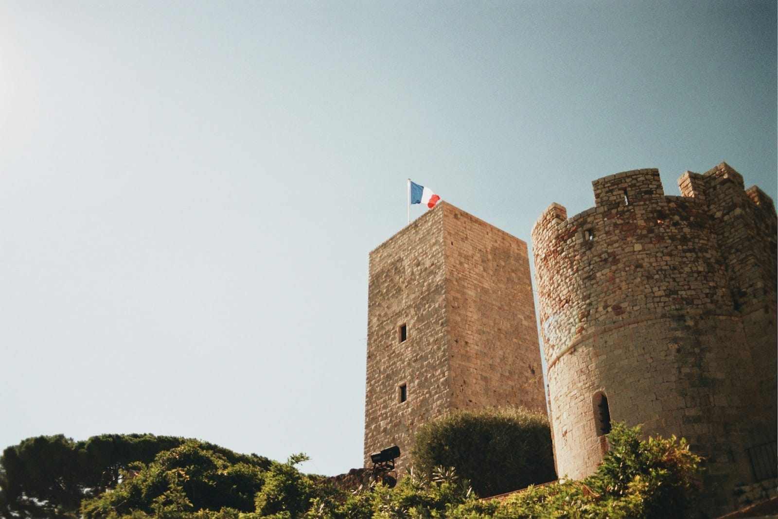 Torre de pedra histórica e torreão redondo de Le Suquet em Cannes, França, sob um céu azul limpo com a bandeira francesa hasteada no topo.
