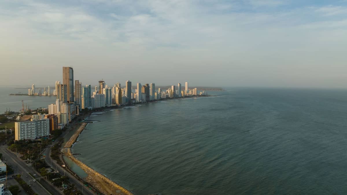 Aerial panorama of Cartagena coastline with high-rise buildings and calm Caribbean Sea under a blue sky.