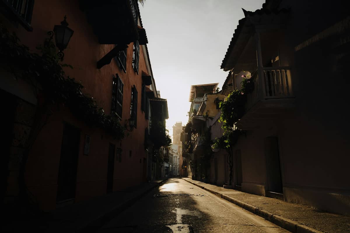 A narrow street in Cartagena with colonial buildings and wet pavement, reflecting the aftermath of a rain shower and evening sunlight.