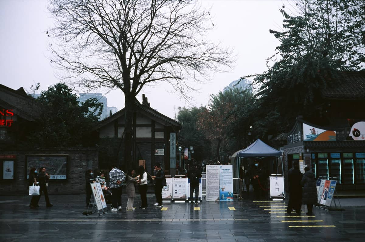Des personnes rassemblées dans une rue piétonne de Chengdu avec des bâtiments de style traditionnel et des panneaux d'information visibles.