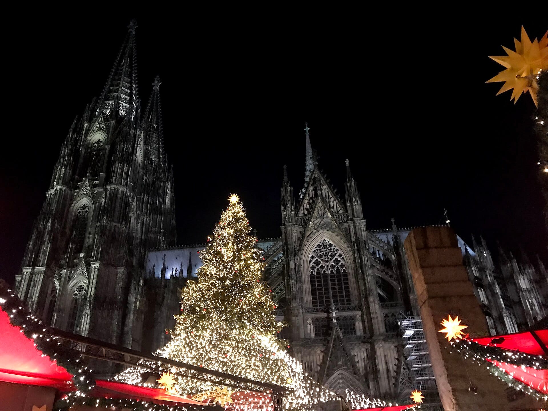 มหาวิหาร Cologne ยามค่ำคืนพร้อมต้นคริสต์มาสที่สว่างไสวและแผงตลาดเทศกาลในเบื้องหน้า