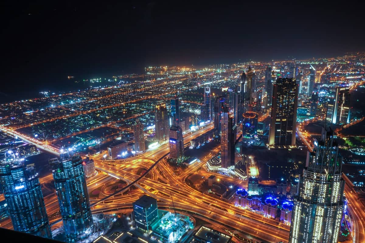 Nächtliche Luftaufnahme von Dubai mit beleuchteten Wolkenkratzern und belebten Highways, die die lebendige städtische Atmosphäre zeigen.
