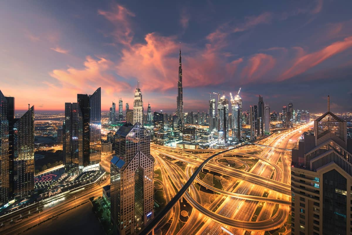 Dramatischer Sonnenuntergang über der Skyline von Downtown Dubai mit Burj Khalifa und Sheikh Zayed Road, Stadtlichtern, Wolkenkratzern und farbenprächtigen Wolken.