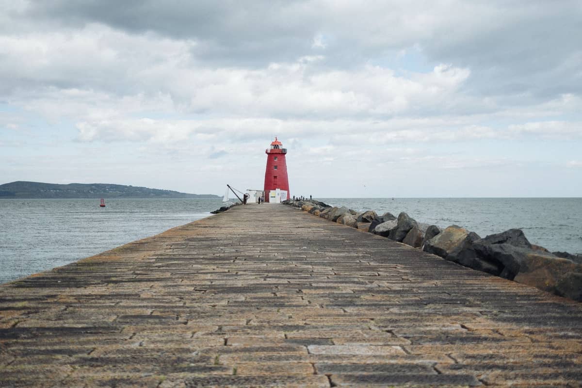Bewölkter Himmel über dem Poolbeg Lighthouse am Ende eines Steinpiers in der Dublin Bay mit Meer und fernen Hügeln