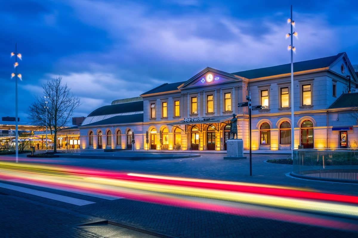 Evening view of Gent-Sint-Pieters railway station in Ghent with illuminated facade and light trails from passing vehicles.
